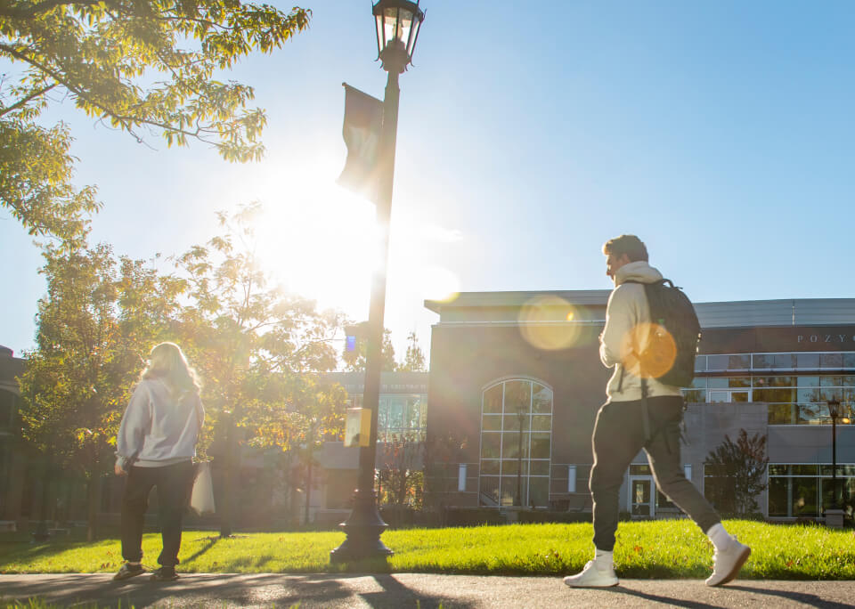 Two students walk while the sun is setting against a blue sky