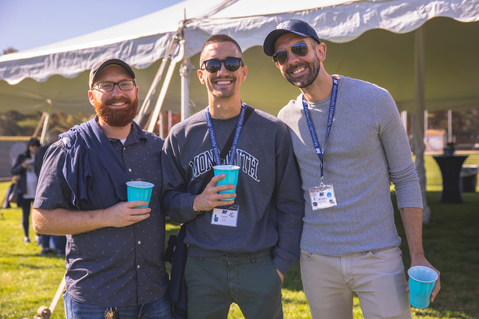 3 alumni in front of tent with drinks