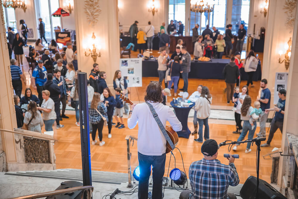Shot from behind a band playing for an audience in the lobby of the Great Hall