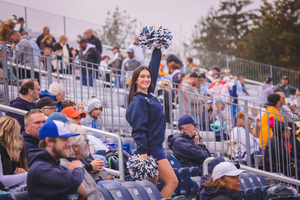 Cheerleader in the stands of Kessler Stadium, arm raised with pom-pom in hand