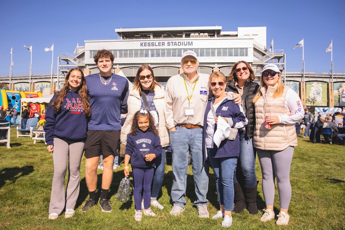 A family in Monmouth gear posing by Kessler Stadium during Homecoming and Reunion Weekend