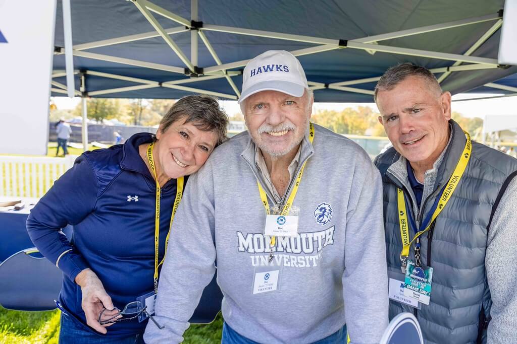 3 volunteers at Homecoming Tailgate check in gathered together and smiling at the camera