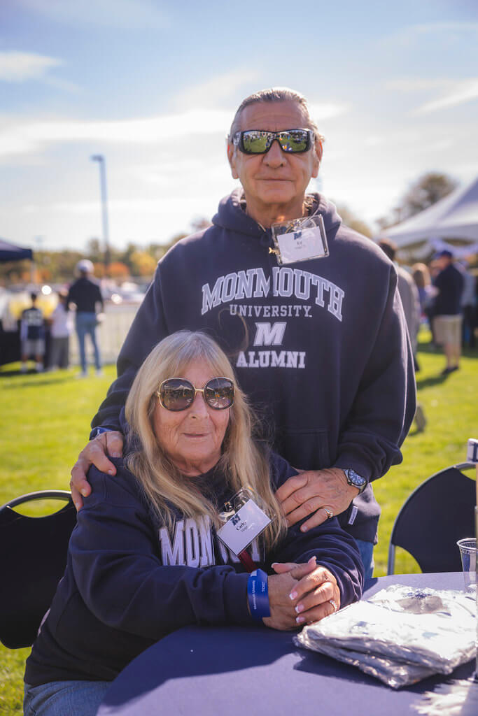 couple wearing monmouth university alumni sweatshirts smiling at the camer