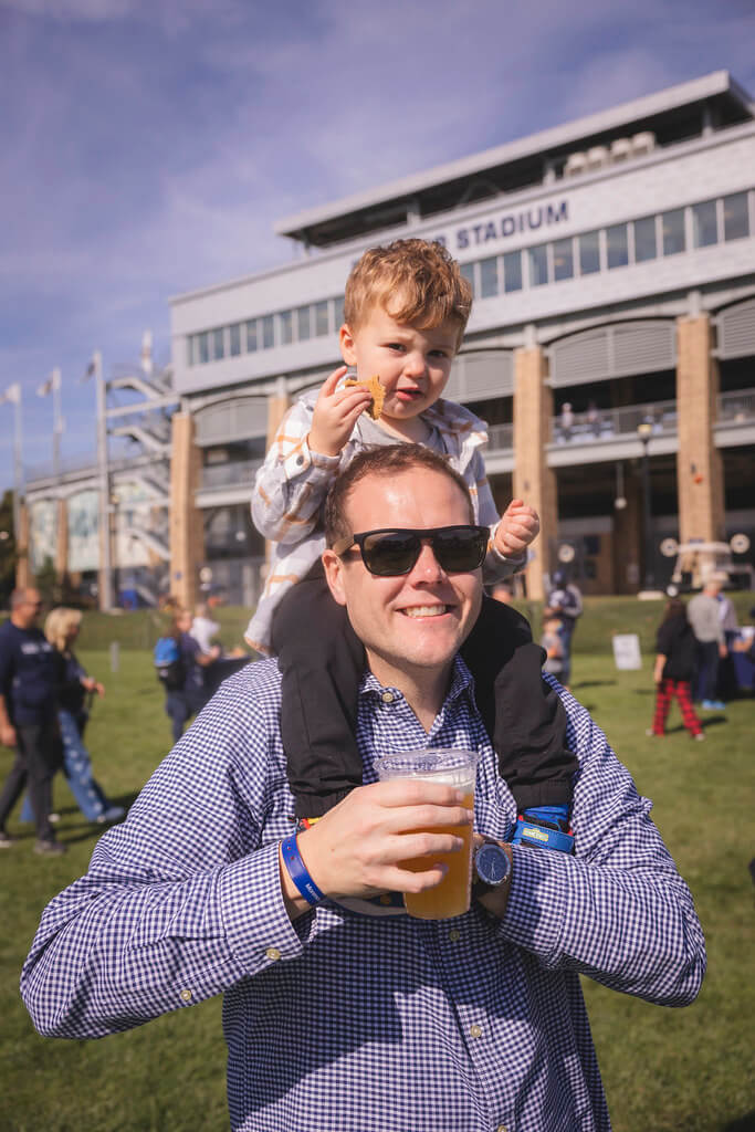 dad holding a beer with his son on his shoulders in front of kessler stadium