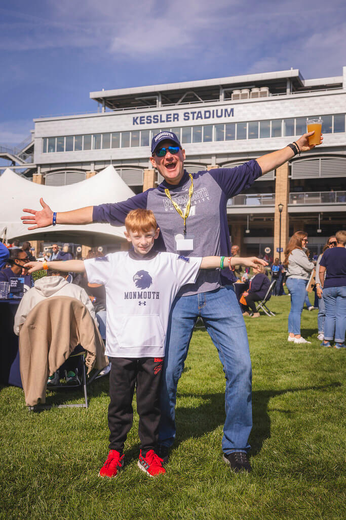 dad and son in monmouth gear in front of Kessler Stadium with their arms wide open