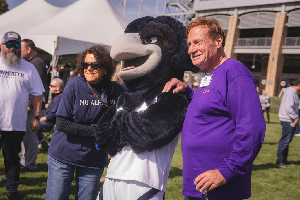 couple standing next to Shadow the Hawk smiling in front of Kessler Stadium