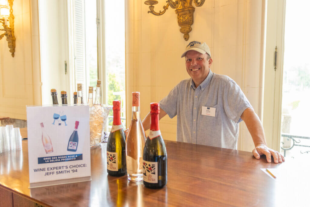 Man standing behind table where three bottles of wine are displayed beside a sign reading “Wine Expert’s Choice: Jeff Smith ’94."