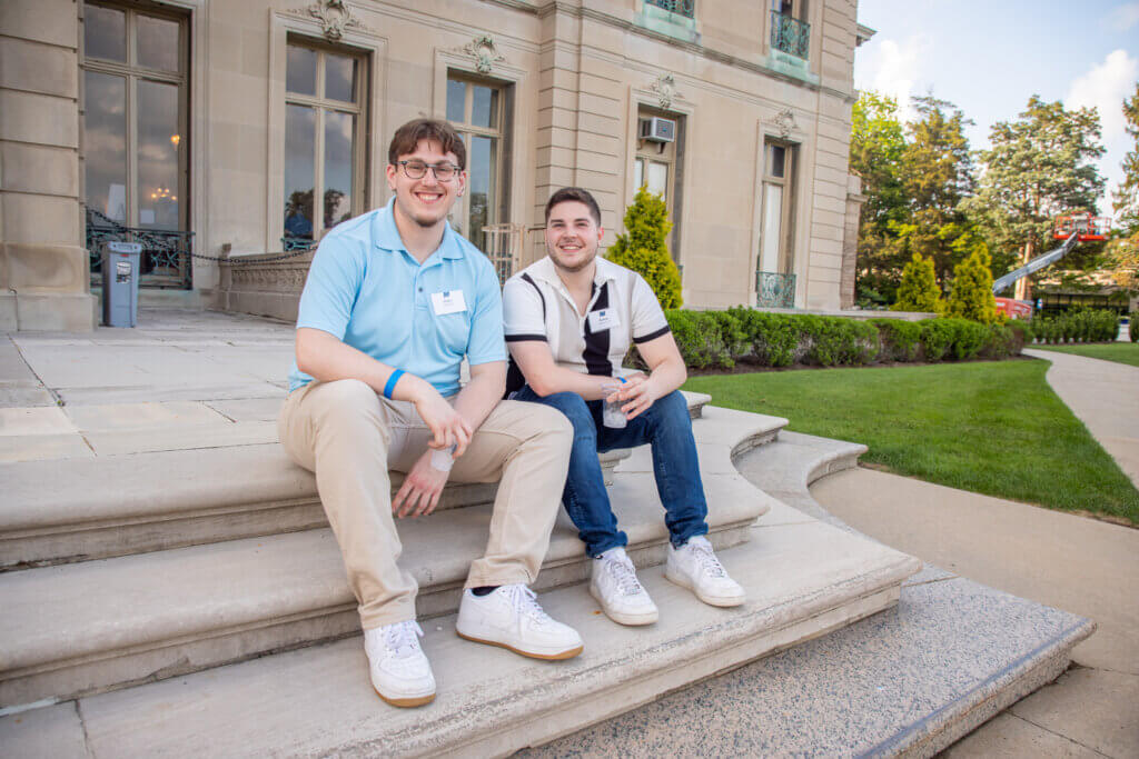 Two alumni smiling for the camera as they enjoy the beautiful atmosphere outside the Great  Hall.