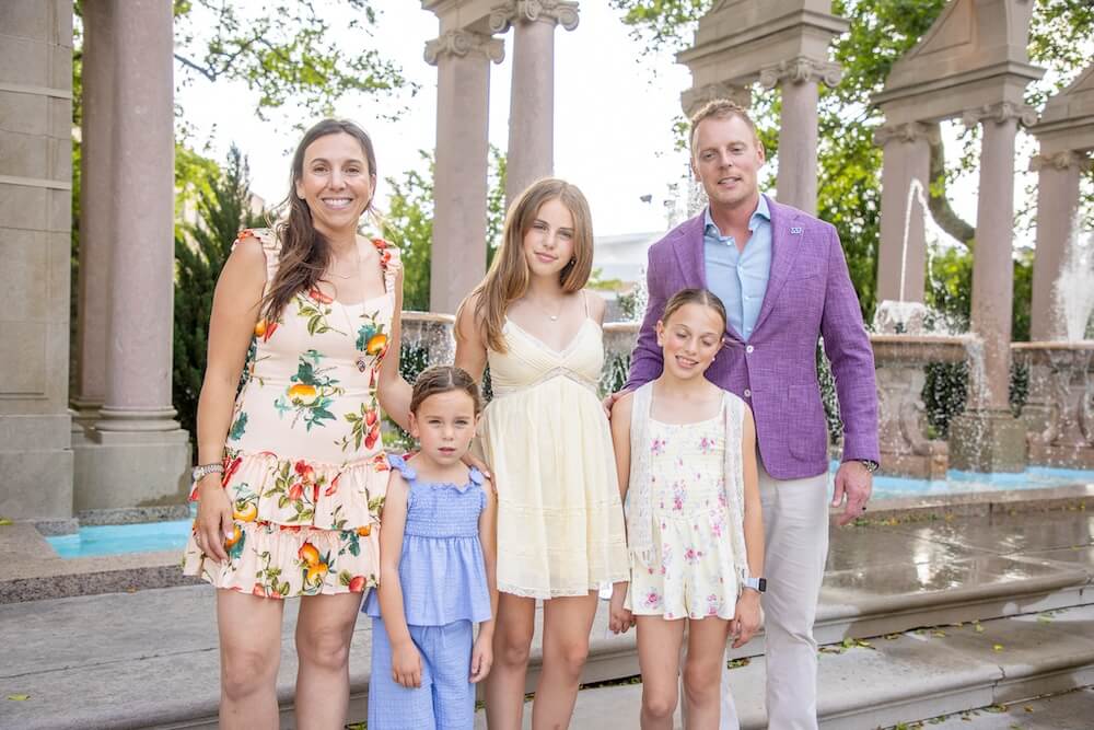 Man, woman and children posing for photo near outdoor fountains in a garden