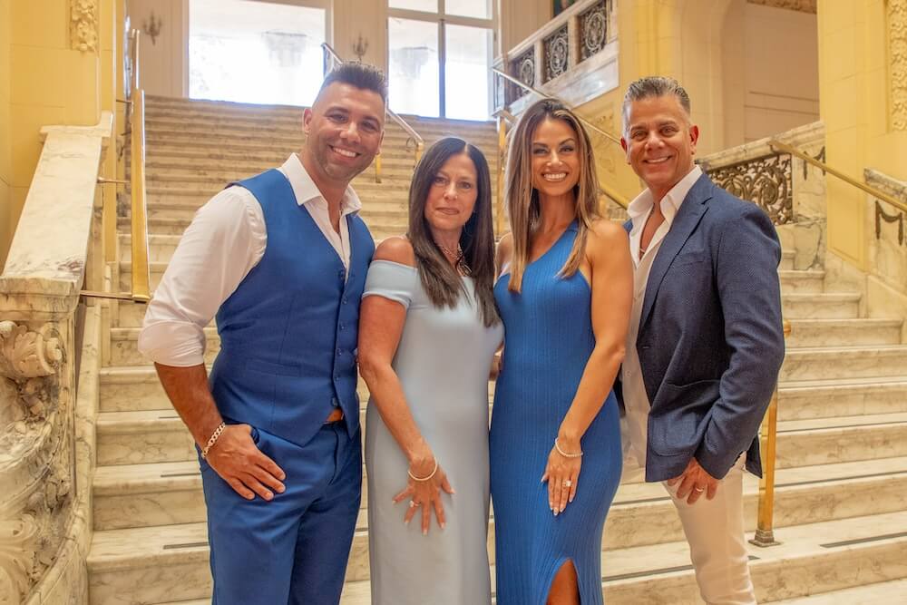 Two men in suits and women in dresses posing for photo on marble steps inside large hall
