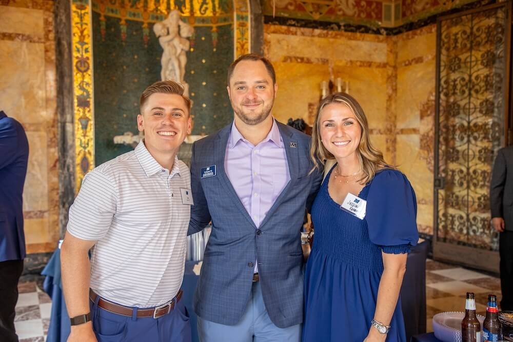 Two men and a woman posing together for photo in room with an indoor fountain.