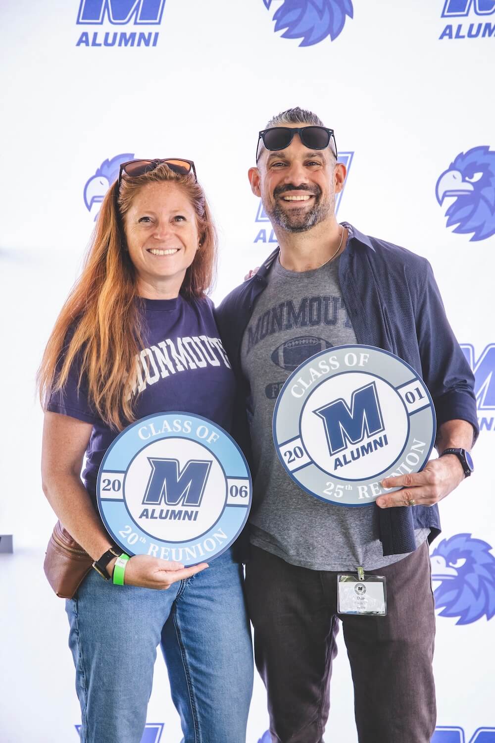 Two alumni smile in front of a Monmouth Alumni backdrop, holding signs for their Class of 2006 20th reunion and Class of 2001 25th reunion.