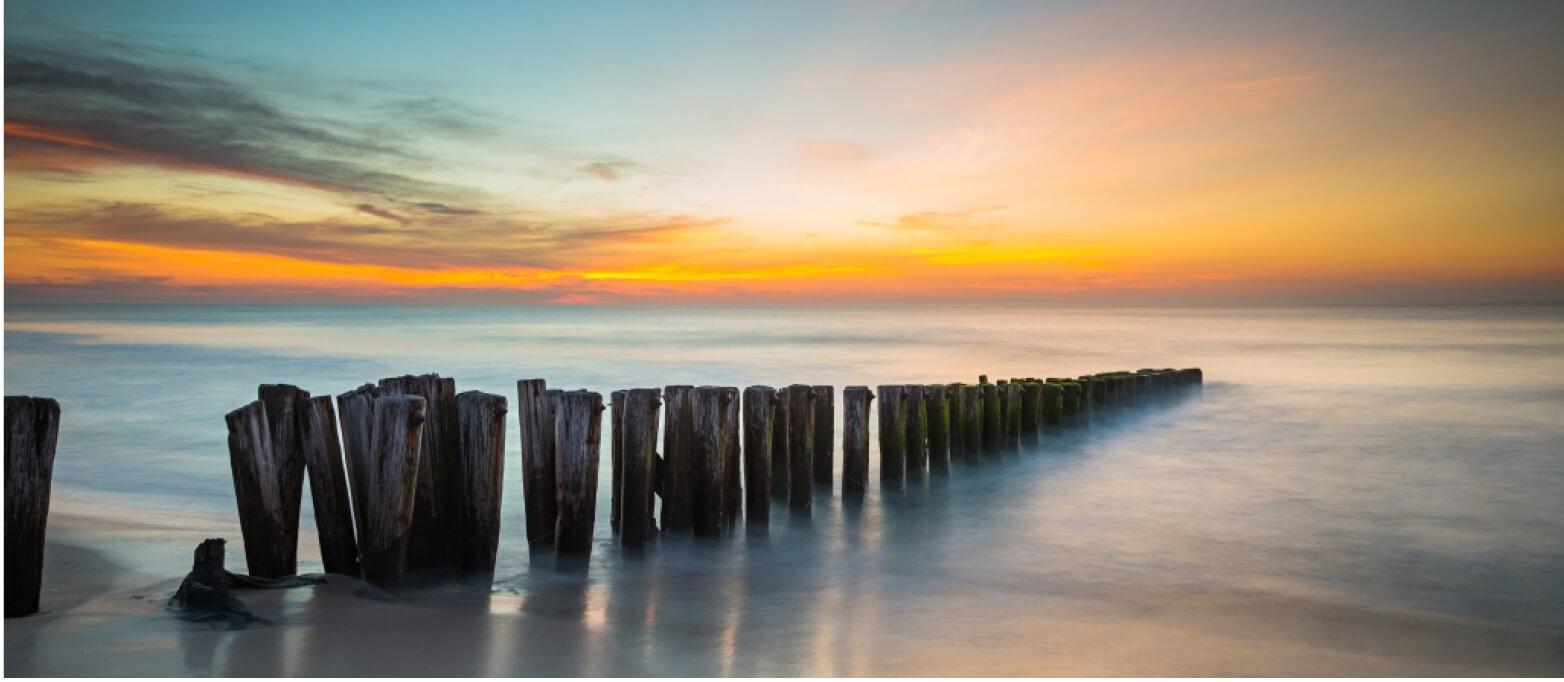 A photo of a sunrise over the ocean with a wooden jetty receding into the ocean. 