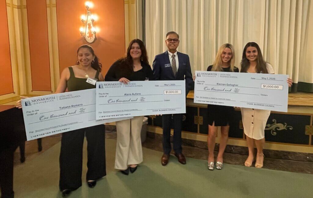 A professional and four students holding three oversized checks, each for $1,000