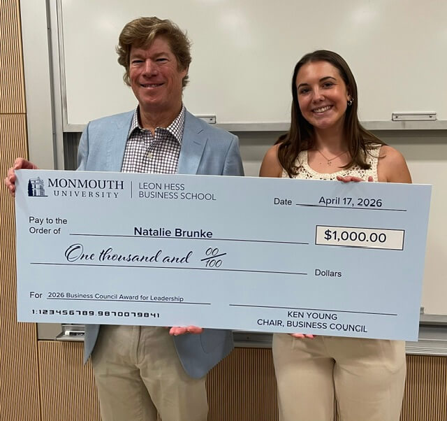 Man and woman holding an oversized check. The check is for $1,000, dated April 17, 2025, and awarded to Natalie Brunk for the 2026 Business Council Award for Leadership. Its from Ken Young, Chair of the Business Council 