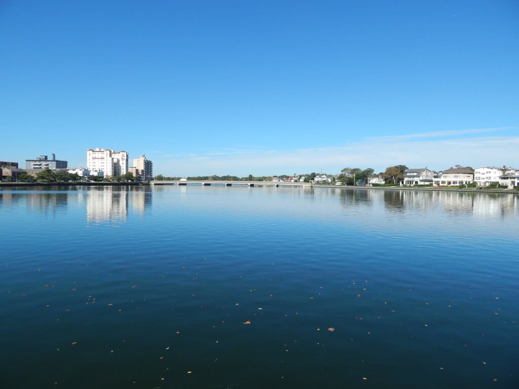 a lake with the blue sky reflecting on it and buildings in the background
