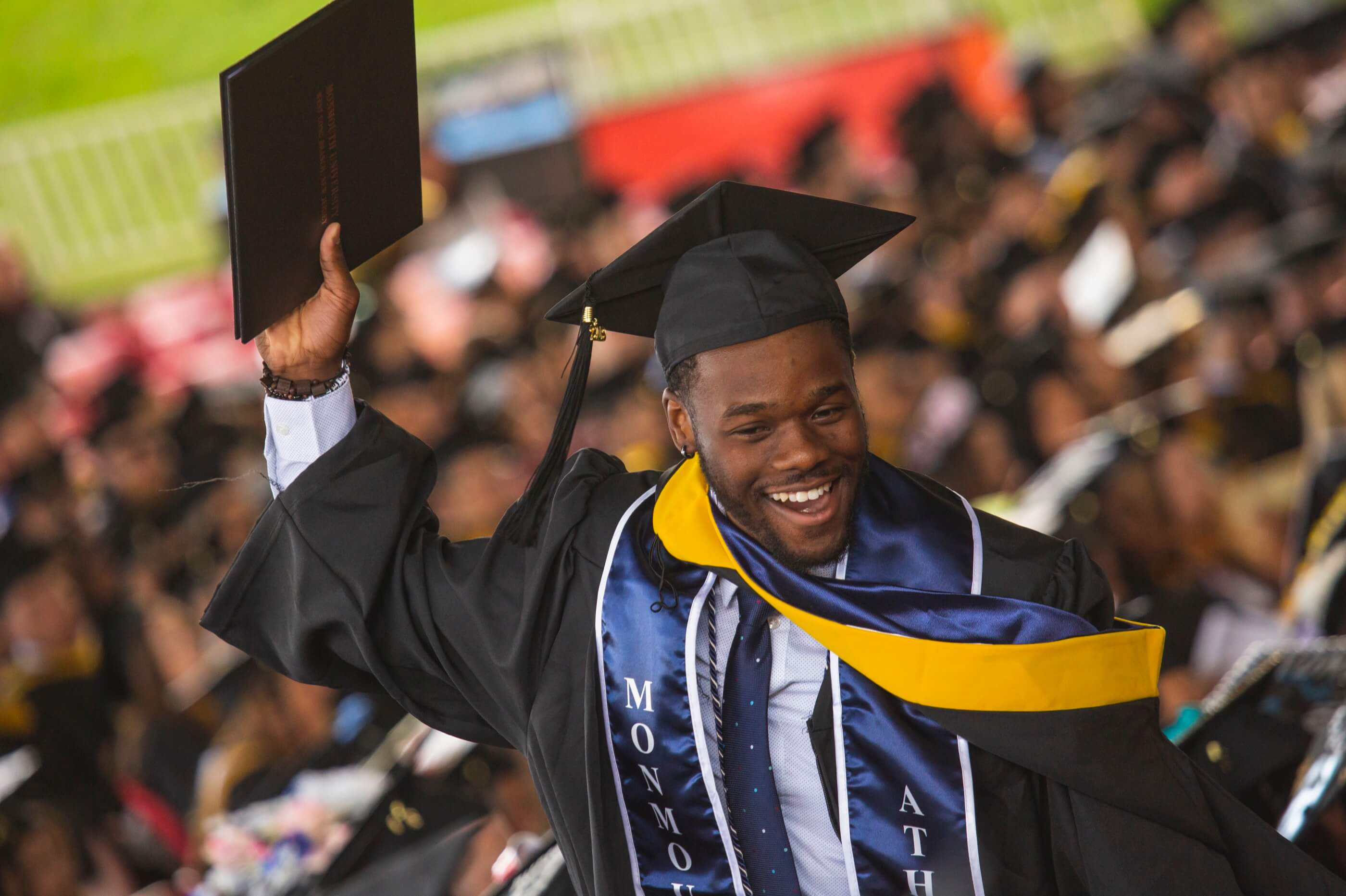 A man is holding a diploma while smiling at commencement.