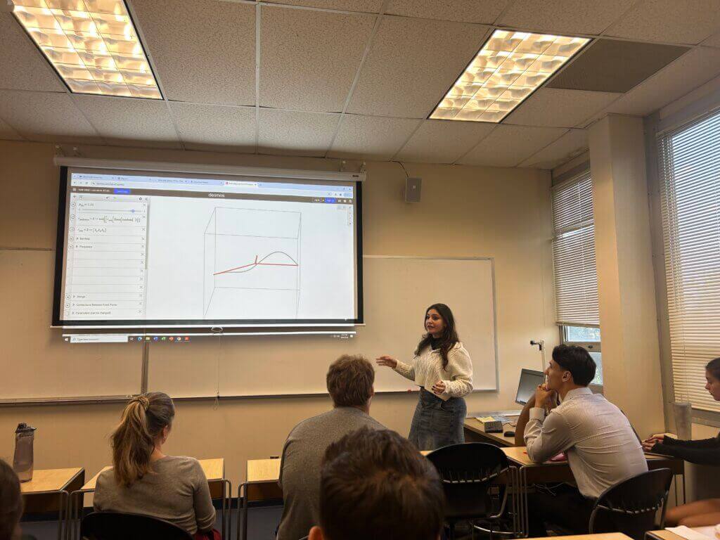 Lecturer presenting to a classroom, using a graph on a computer.