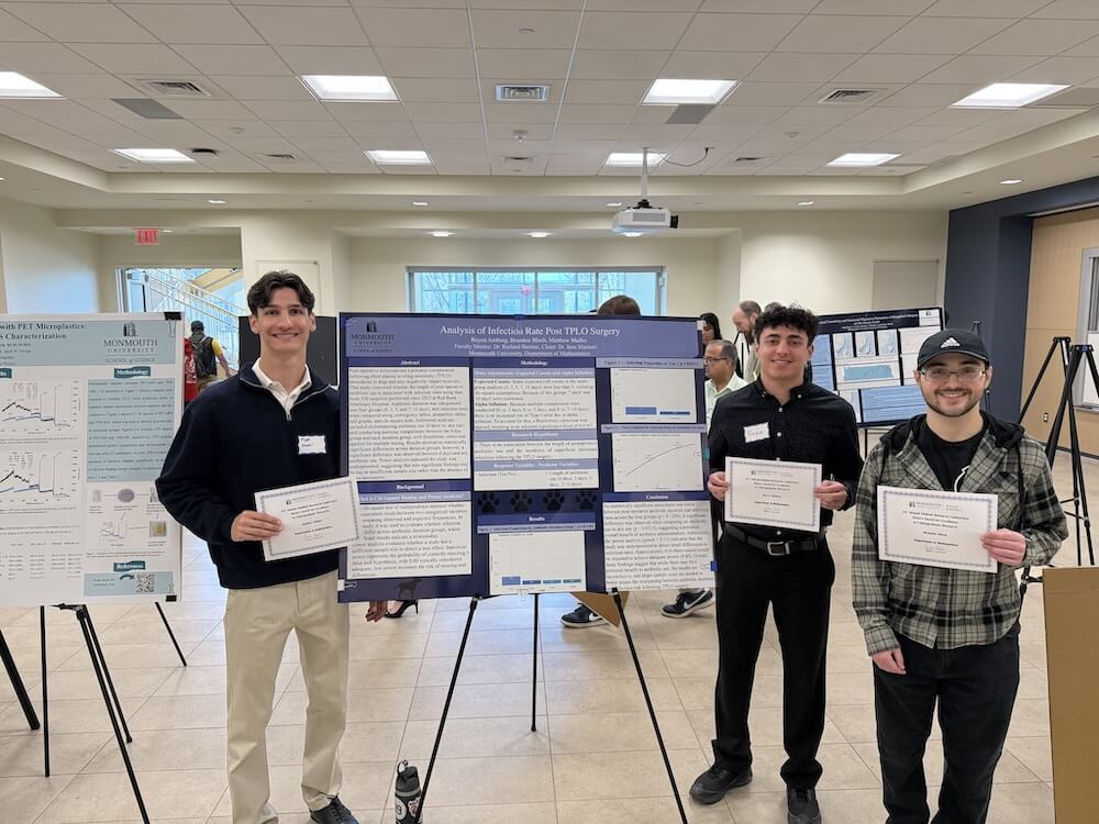 Three students hold certificates near poster presentation