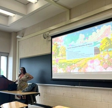 Woman presenting in a classroom, screen showing slide with illustration of mountains and greenery