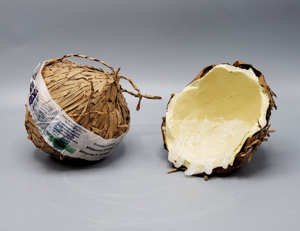 Sculptural object resembling a split fruit, made of shredded brown paper and packaging material with a pale, translucent interior.
