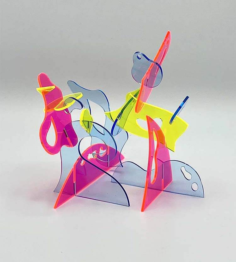 Bright abstract sculpture made of translucent pink, yellow, blue, and clear acrylic shapes interlocked into an airy tabletop composition.
