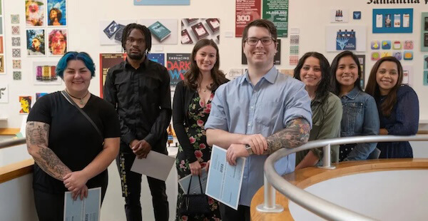 Students standing in front of wall adorned with art pieces.