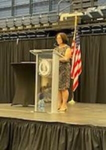 Woman speaking at glass podium with American flag behind her