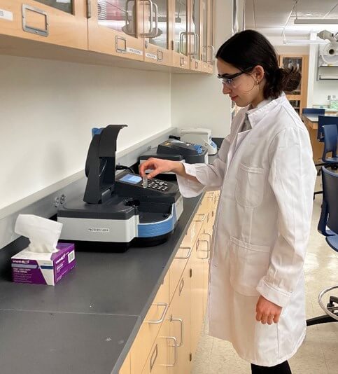 Woman in lab coat placing a beaker inside a high-tech piece of equipment