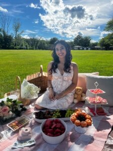 Woman sitting on picic blanket with an assortment of food and flowers surrounding her