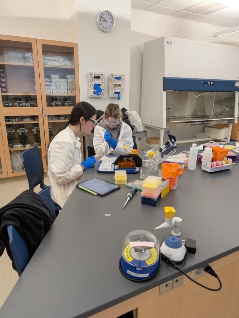 Students in white coats performing an experiment at a lab table