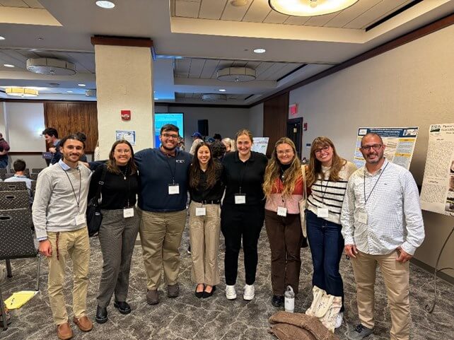 Men and women wearing lanyards, standing side by side with arms around each other's shoulders, smiling