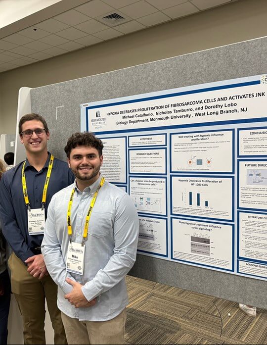 Two students wearing lanyards standing in front of a poster presentation