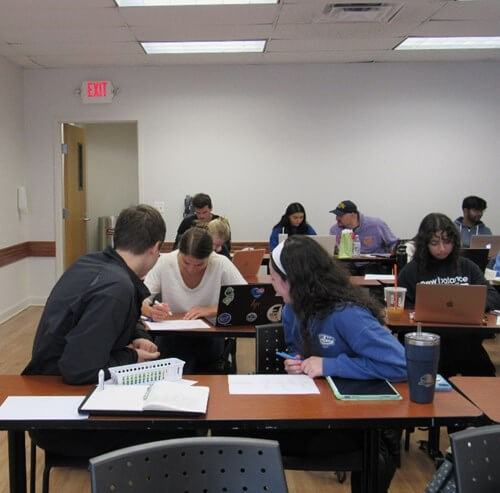 A classroom full of students, all either talking among themselves or taking notes