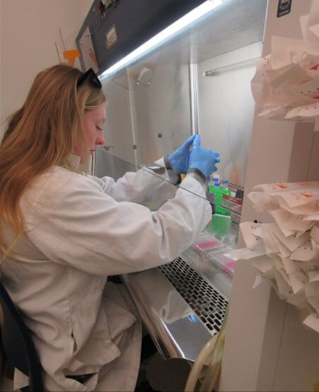 Woman in white lab coat and blue rubber gloves handling chemicals