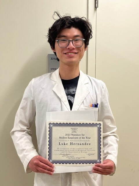 Young man in white coat holds up certificate. It reads "2025 Nominee for Student Employee of the Year Luke Hernandez"