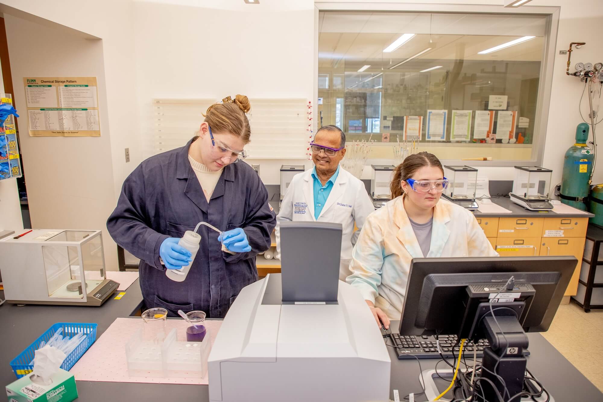 Two students and professor using advanced equipment in chemistry lab