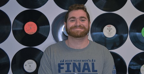 Sean Gerhard smiling in front of hung vinyl records