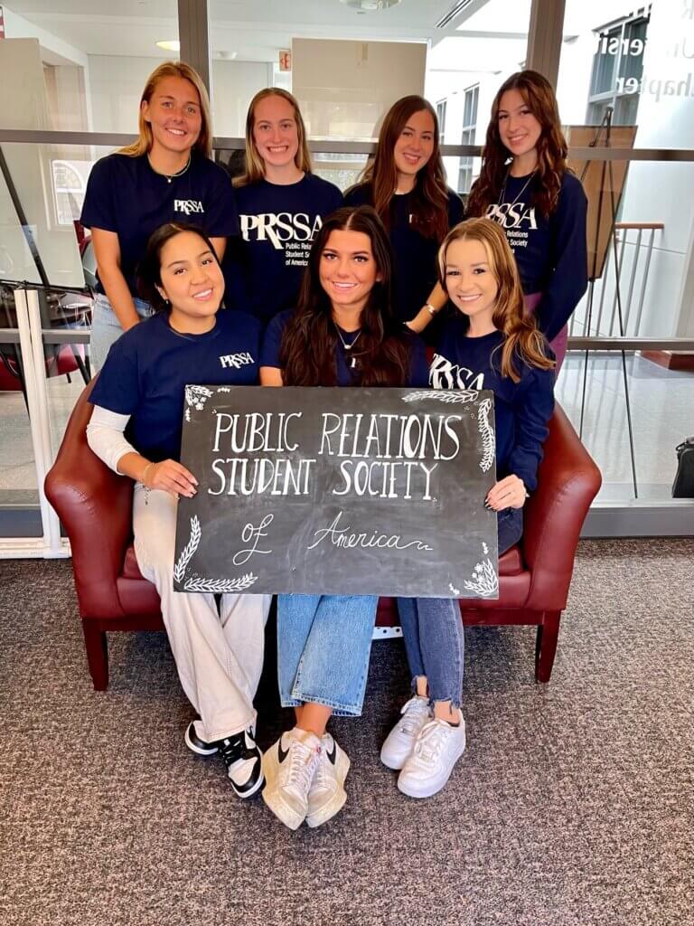 PRSSA Members holding a board that says "Public Relations Student Society of America"