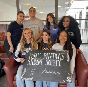 PRSSA Members holding a board that says "Public Relations Student Society of America"