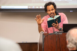 Man at podium reading book aloud for audience