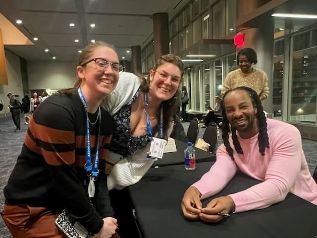 Two women and a man pose for a photo at a table.