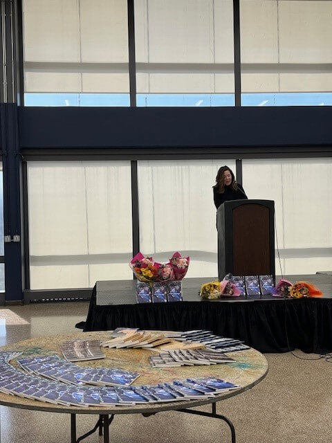 Woman speaking at podium, with journals laid out on a table.