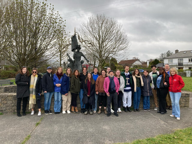 Large group of people posing for photo in front of a park statue