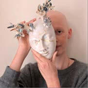Poet holding mask with flowers on forehead