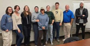 Eight students and an older man in a polo smiling for a photo.
