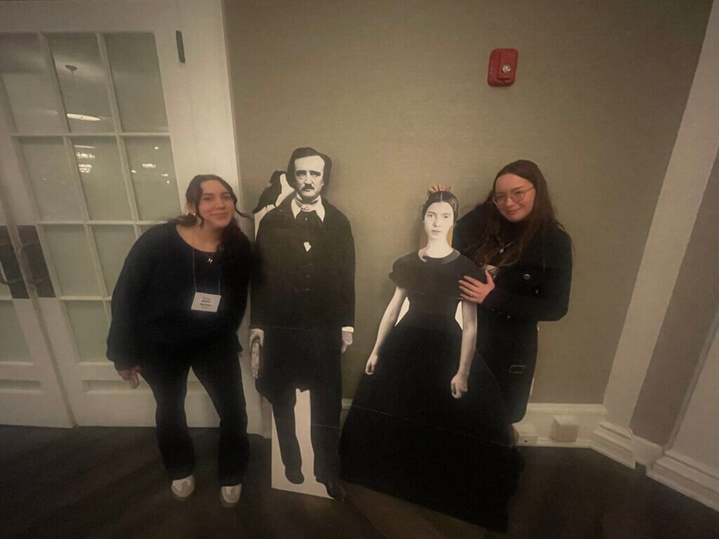 Women standing near cut outs of famous authors (Edgar Allen Poe and Emily Dickinson)