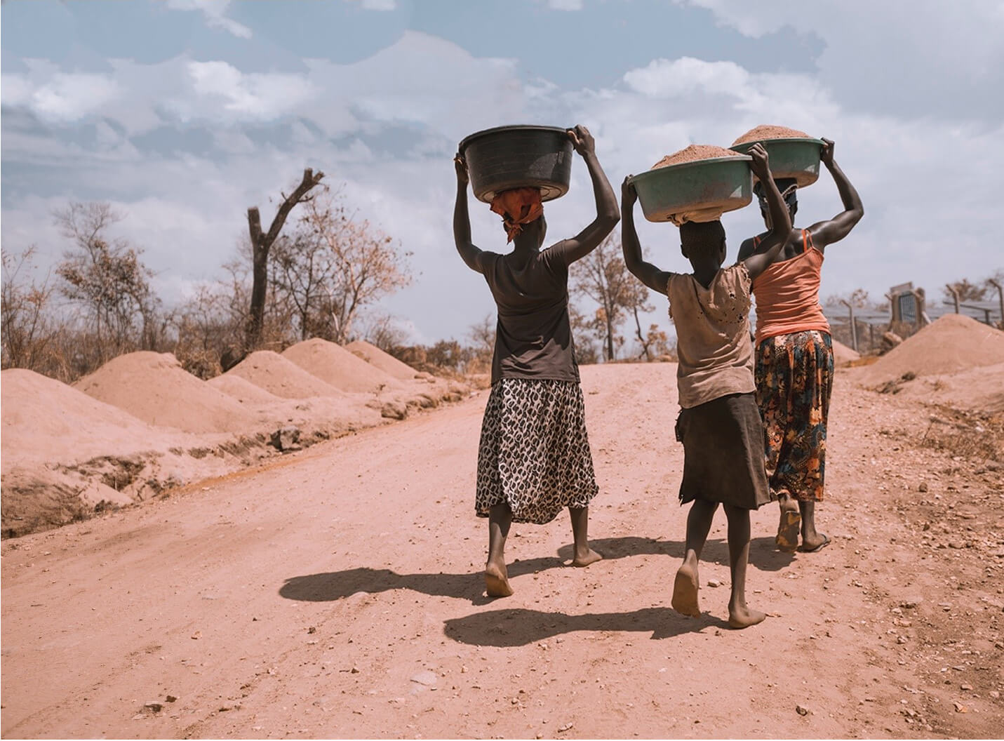 Photo of people in Africa waling along a dirt road while carrying baskets on their heads