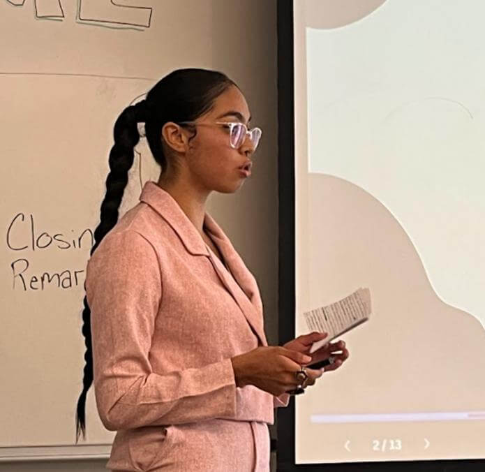 Student delivering a presentation, written notes in her hand.