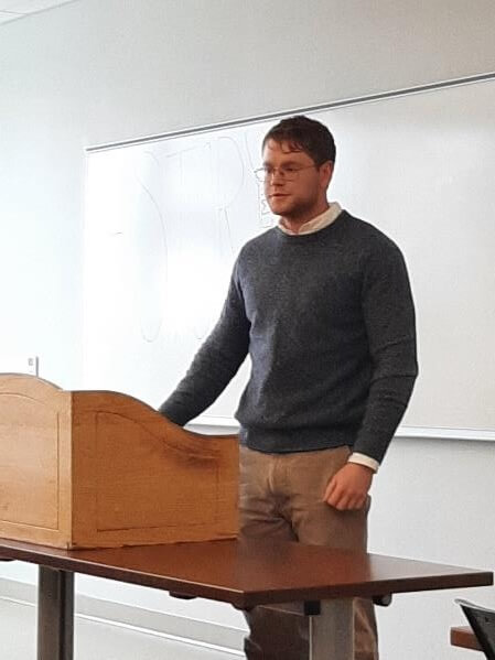 Man speaking at podium in front of a white board